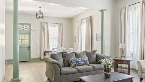 A living room with a grey sofa, a coffee table, and a vase of flowers. There is a door and a window with curtains.