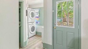 A laundry room with stacked washers and dryers, a door with a window, and a view of trees outside.