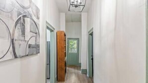 A narrow hallway with wooden flooring, a green door at the end, and a large abstract painting on the left wall.