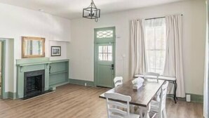 A room with a wooden floor, a dining table with chairs, a fireplace, and a green door.