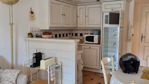 A compact kitchen with white cabinets, a microwave, and a small refrigerator. There is a dining table with chairs and a coffee machine. - Beautiful, comfortable vacation apartment for 4 people in Cavalaire sur Mer. (Cavalaire-sur-Mer)