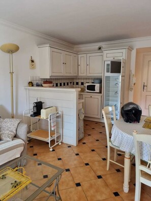 A compact kitchen with white cabinets, a microwave, and a small refrigerator. There is a dining table with chairs and a coffee machine. - Beautiful, comfortable vacation apartment for 4 people in Cavalaire sur Mer. (Cavalaire-sur-Mer)