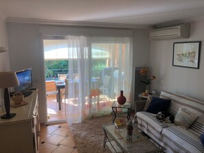 Een woonkamer met een bank, een salontafel, een televisie en een balkon met een tafel en stoelen.