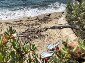 A beach with driftwood, a rocky outcrop, and two striped beach chairs. - Beautiful, comfortable vacation apartment for 4 people in Cavalaire sur Mer. (Cavalaire-sur-Mer)