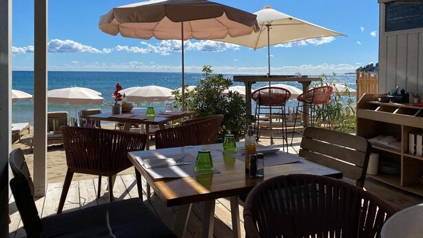 An outdoor patio with wooden tables and chairs, large umbrellas, and a view of the ocean. - Beautiful, comfortable vacation apartment for 4 people in Cavalaire sur Mer. (Cavalaire-sur-Mer)