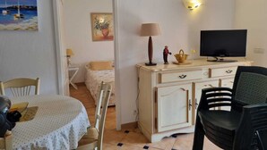 A room with a bed, a television, a dining table with chairs, and a small cabinet. - Beautiful, comfortable vacation apartment for 4 people in Cavalaire sur Mer. (Cavalaire-sur-Mer)
