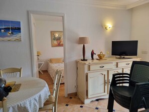 A room with a bed, a television, a dining table with chairs, and a small cabinet. - Beautiful, comfortable vacation apartment for 4 people in Cavalaire sur Mer. (Cavalaire-sur-Mer)