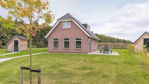 Une maison en briques avec un toit en pente, un petit porche et une pelouse.