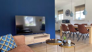 Un salon doté d’un grand téléviseur à écran plat, d’un canapé, d’une table basse et d’un coin repas avec des chaises et une table.