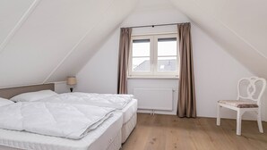 Une chambre à coucher avec un lit, une chaise, une fenêtre avec des rideaux et un radiateur.