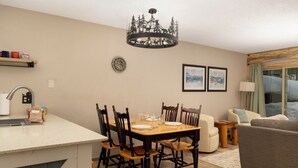 Comedor con una mesa de madera dispuesta para seis personas, rodeada de sillas. Un candelabro cuelga sobre la mesa.