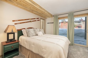 Une chambre à coucher avec un lit, une table de chevet, une lampe et une vue sur l’extérieur.