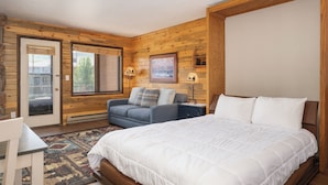 Een slaapkamer met een groot bed, een bank, een bureau en een deur naar een balkon.