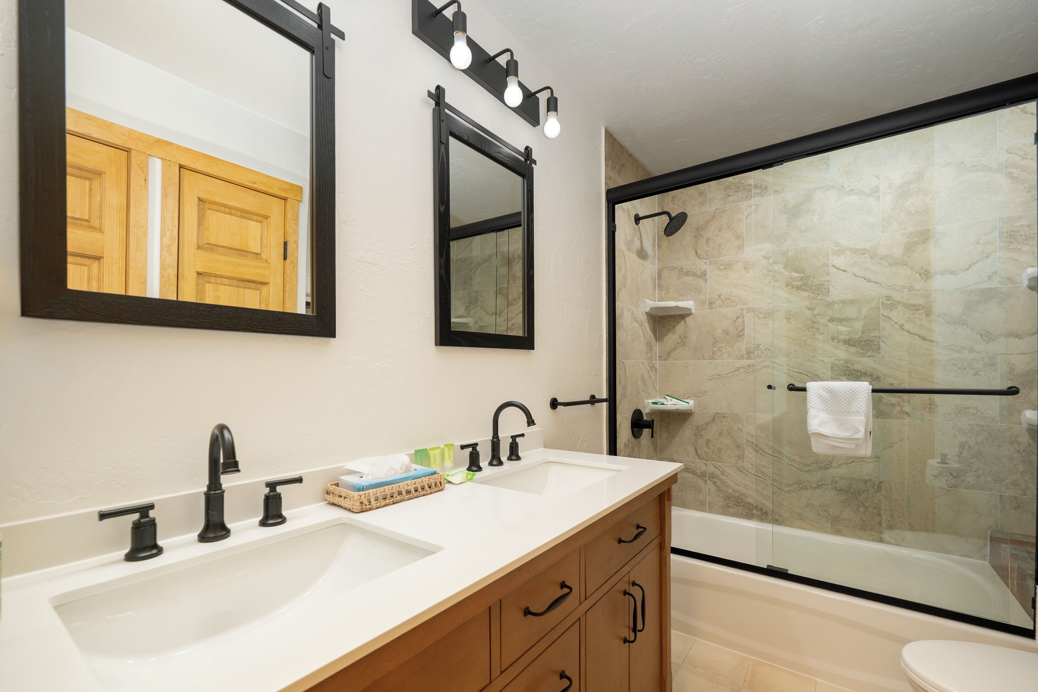 A modern bathroom with a large mirror, two sinks, and a glass-enclosed shower.