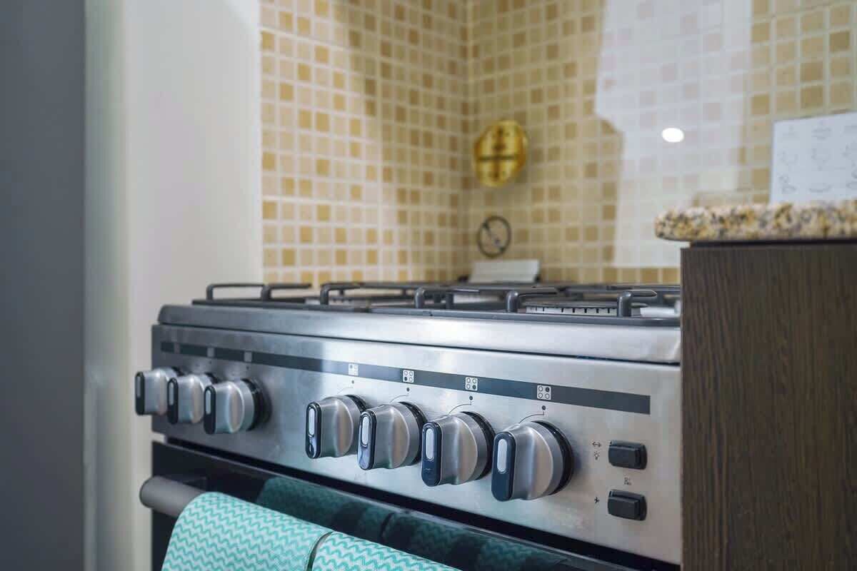 Een keuken met een gasfornuis, een betegelde spatwand en een houten kast.
