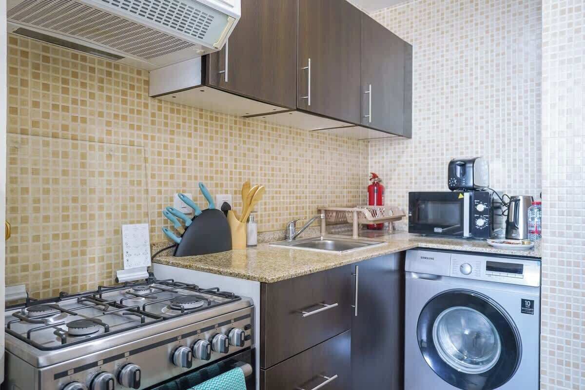 Een praktische keuken met een gasfornuis, magnetron en wasmachine.