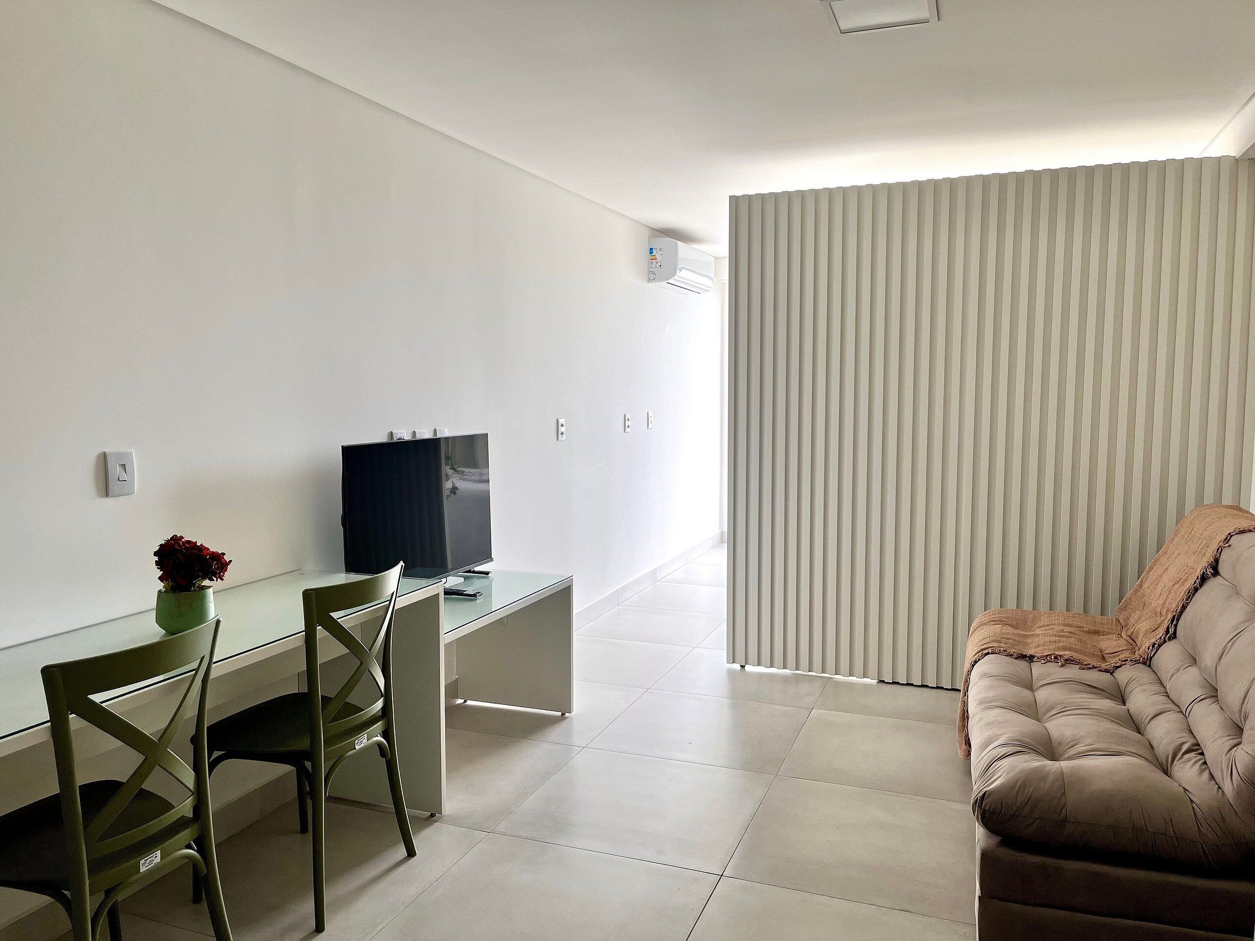 Ein modernes Wohnzimmer mit einem Glastisch, einem Flachbildfernseher, einem grünen Sessel, einem beigen Sofa und einem gestreiften Vorhang.