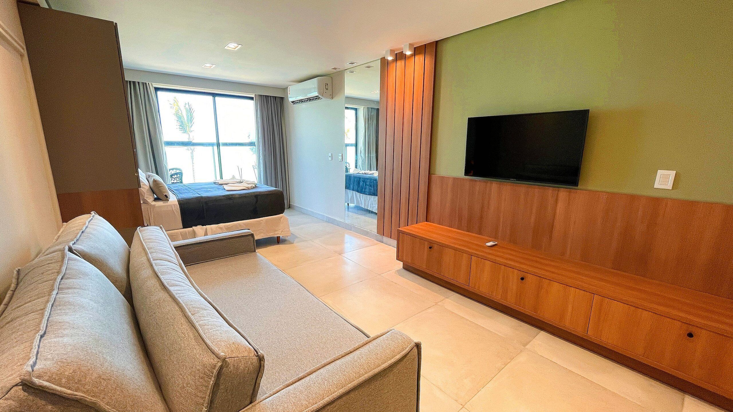 Ein modernes Wohnzimmer mit einer Couch, einem an der Wand montierten Fernseher und einem Bett im Hintergrund.