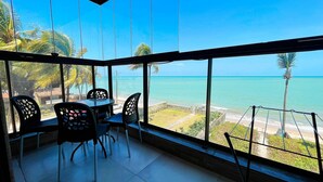 Habitació amb una finestra gran que dona a una platja. Hi ha una taula amb cadires i vista a l'oceà.