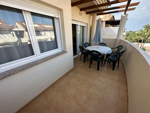 A balcony with a table and chairs, a pergola, and a view of neighboring buildings. - Apartamento Playa Sol A - Apartment with pool in Vinaròs (Vinaròs)
