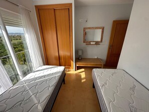 A bedroom with two single beds, a wooden wardrobe, a small bedside table, a mirror, and a window with curtains. - Apartamento Playa Sol A - Apartment with pool in Vinaròs (Vinaròs)