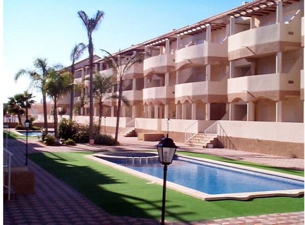 A hotel with a swimming pool, palm trees, and a building with balconies. - Apartamento Playa Sol A - Apartment with pool in Vinaròs (Vinaròs)