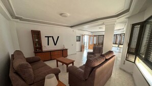 A spacious living room with two brown sofas, a wooden coffee table, and a TV mounted on the wall.