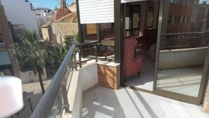 A balcony with a red chair, a glass door leading to a room, and a view of the cityscape.
