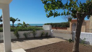 A covered outdoor area with a view of the sea, a tree, and a white wall with a gate.