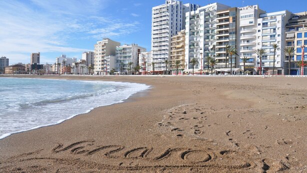 A beach with footprints spelling "Venice" in the sand, surrounded by modern buildings and palm trees.