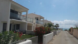A residential street with modern houses, a gated entrance, and a clear view of the sea.