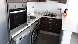 Een kleine keuken met een ingebouwde oven, een wasmachine en een spoelbak.