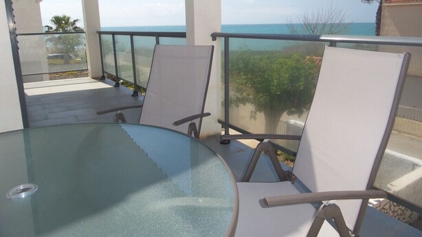 Een balkon met een glazen tafel en twee stoelen, met uitzicht op de kust.