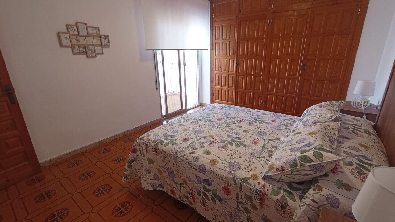 Un dormitorio con colcha estampada, un armario de madera y una puerta corredera de cristal que da a un área exterior.