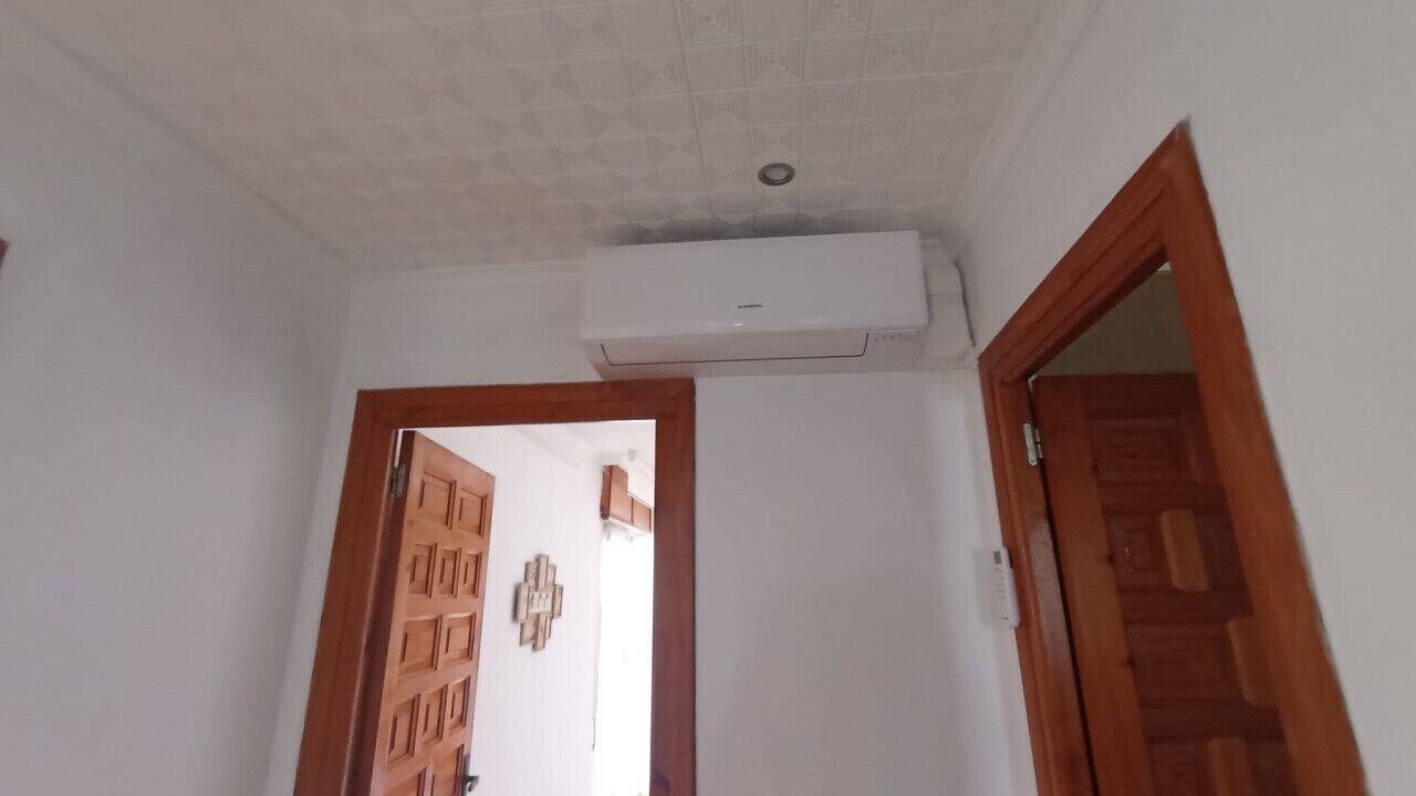 Une pièce avec un plafond blanc, un appareil de climatisation, un chambranle de porte en bois et une porte en bois.