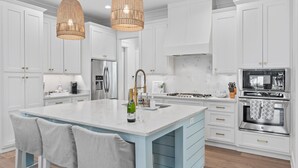 Une cuisine moderne avec des meubles blancs, un grand îlot central, des appareils en acier inoxydable et des suspensions en osier.