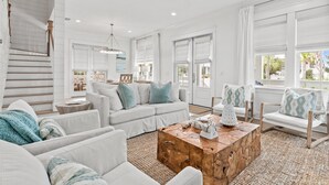 Un salon spacieux, doté d’un canapé blanc, d’une table basse en bois et de grandes fenêtres offrant une vue sur l’extérieur.