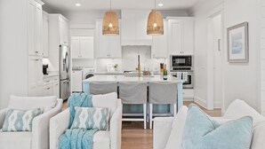 Une cuisine moderne avec des meubles blancs, un îlot central et des luminaires suspendus.