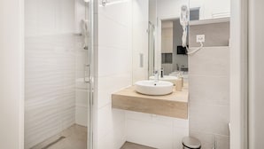 Un baño moderno con cabina de ducha de vidrio, un lavamanos blanco y un espejo con secador de pelo.