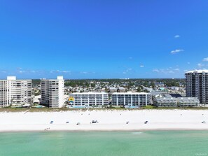 Un hôtel situé en bord de mer, composé de plusieurs bâtiments, avec une plage de sable fin et un ciel d’un bleu éclatant.