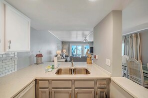 A modern kitchen with a double sink, white cabinets, and a view into the living room.
