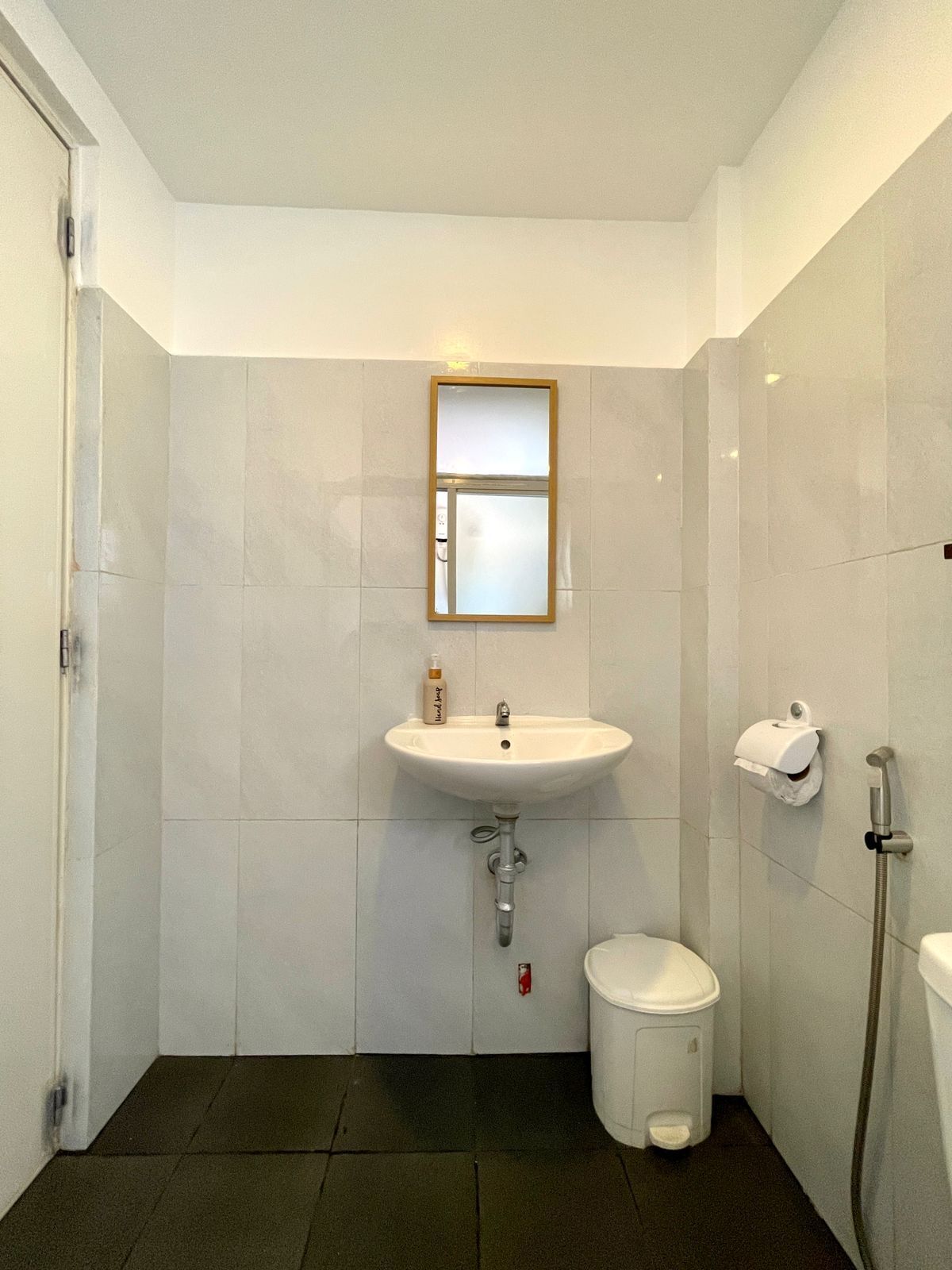 A small, clean bathroom with a white sink, a mirror, a toilet, and a trash bin.