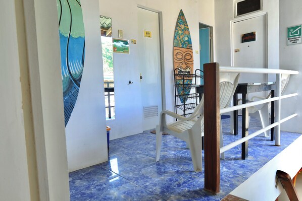 A hallway with a blue-tiled floor, white walls, and a surfboard decoration. There are signs indicating a smoking area and a designated smoking area. - CHILL OUT HOSTEL BORACAY (Boracay Island)