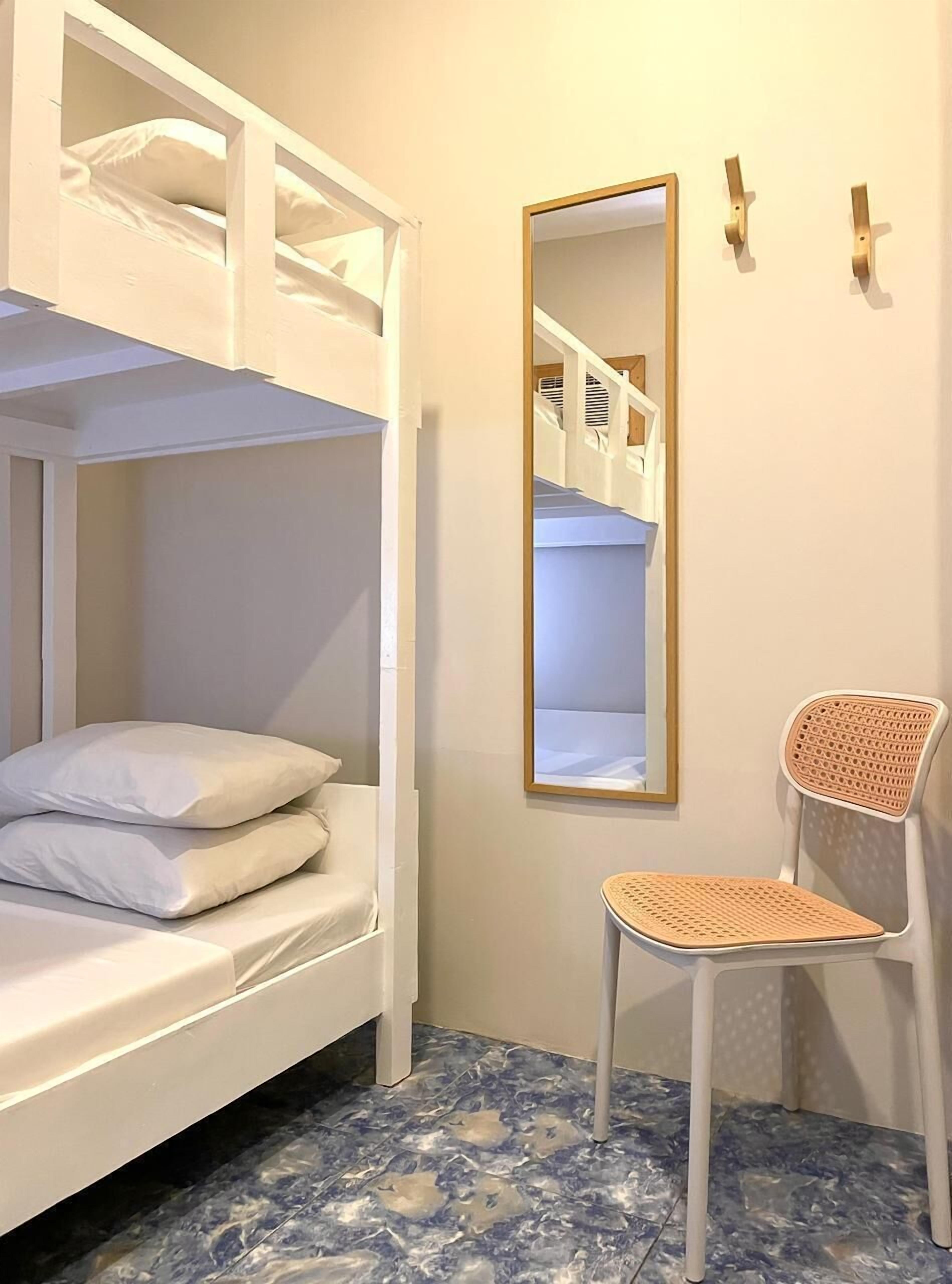 Una cama literaria con almohadas, una silla con respaldo de mimbre y un espejo en la pared.