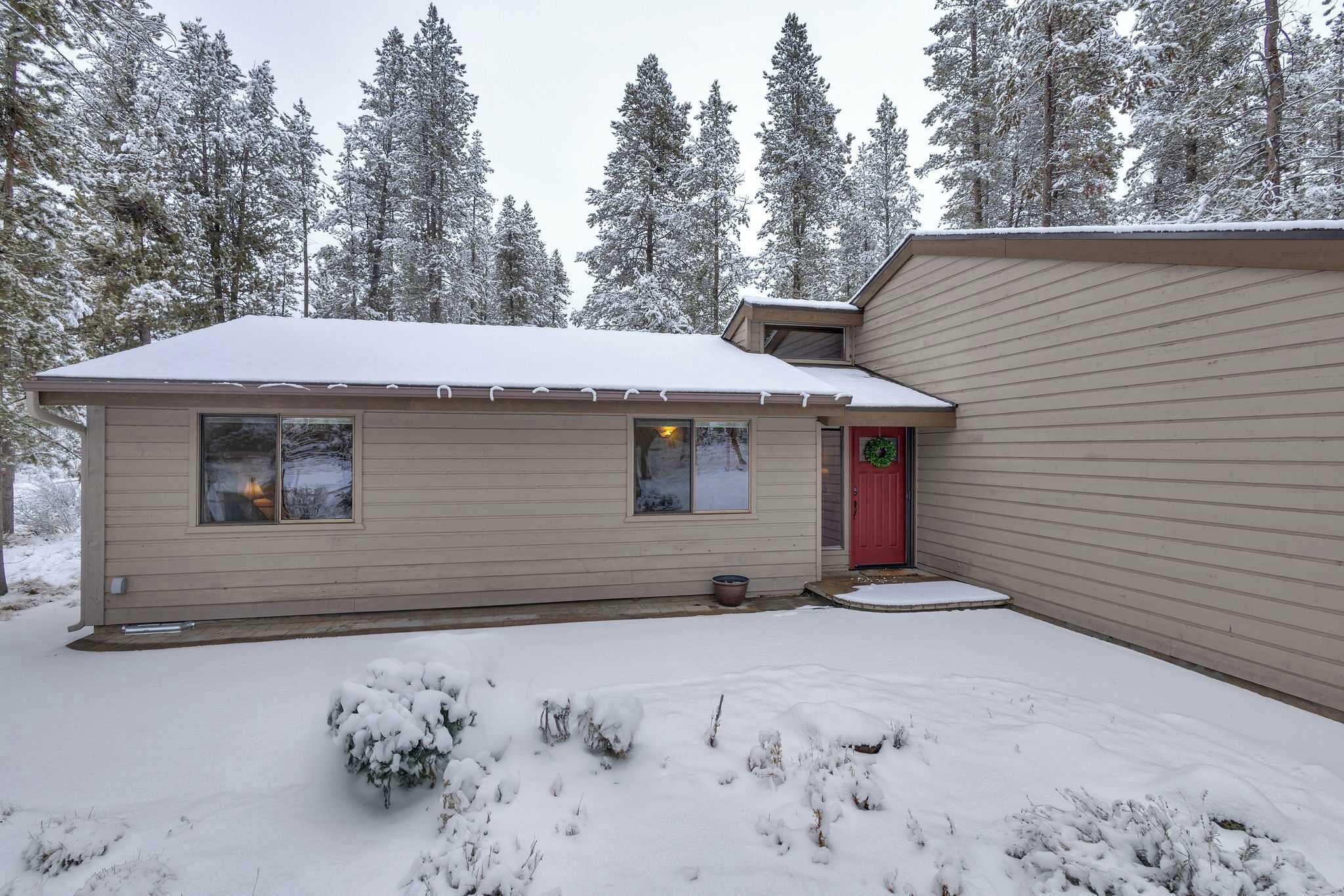Una casa de un piso con una puerta roja, un porche delantero y un patio cubierto de nieve.