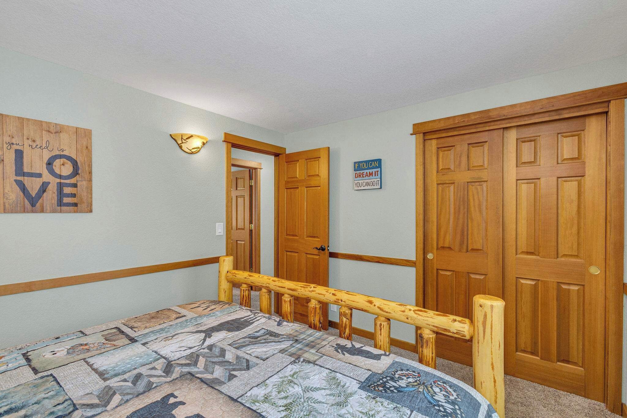 A bedroom with a bed, wooden doors, a wall with motivational quotes, and a patterned rug.