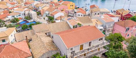 Un pueblo costero con edificios de tejados de terracota, un puerto deportivo con barcos y una ladera cubierta de vegetación.