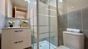 A modern bathroom with a glass shower enclosure, a toilet, and a vanity with drawers.