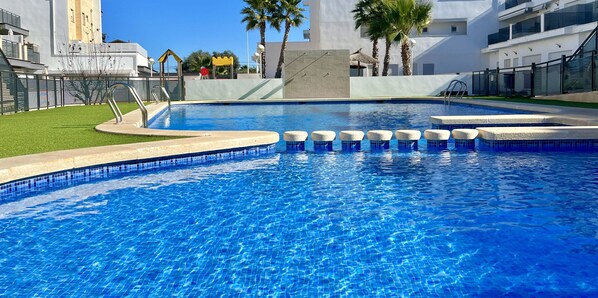 A modern swimming pool with clear blue water, surrounded by a well-maintained lawn and palm trees.