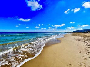 A beach with clear blue water, a sandy shore, and a clear sky.